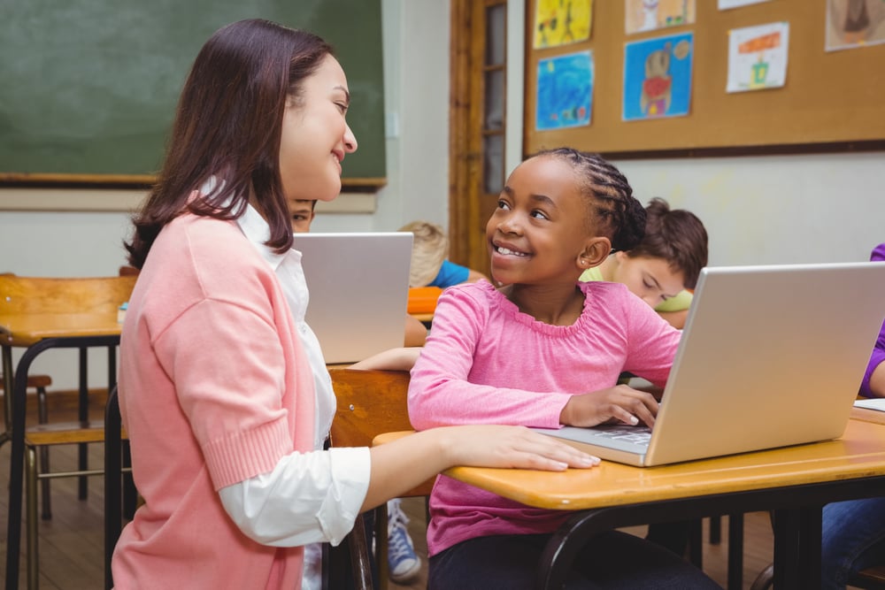 Happy-teacher-using-laptop-with-student-at-elementary-school