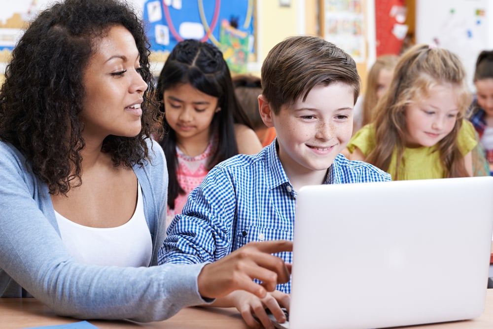 Teacher-Helping-Male-Elementary-Pupil-In-Computer-Class
